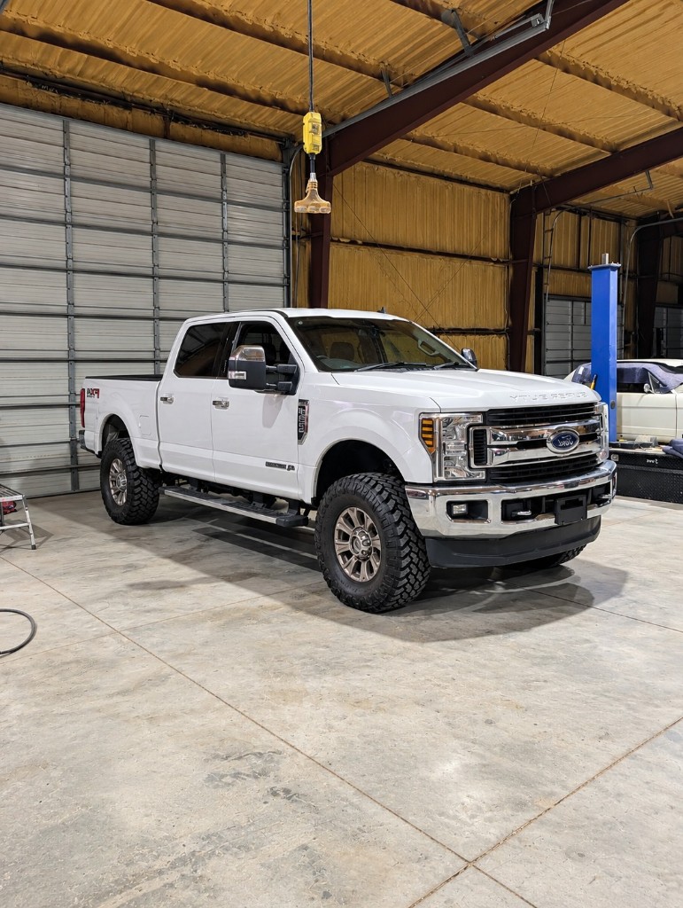 White heavy-duty crew-cab pickup inside a repair shop