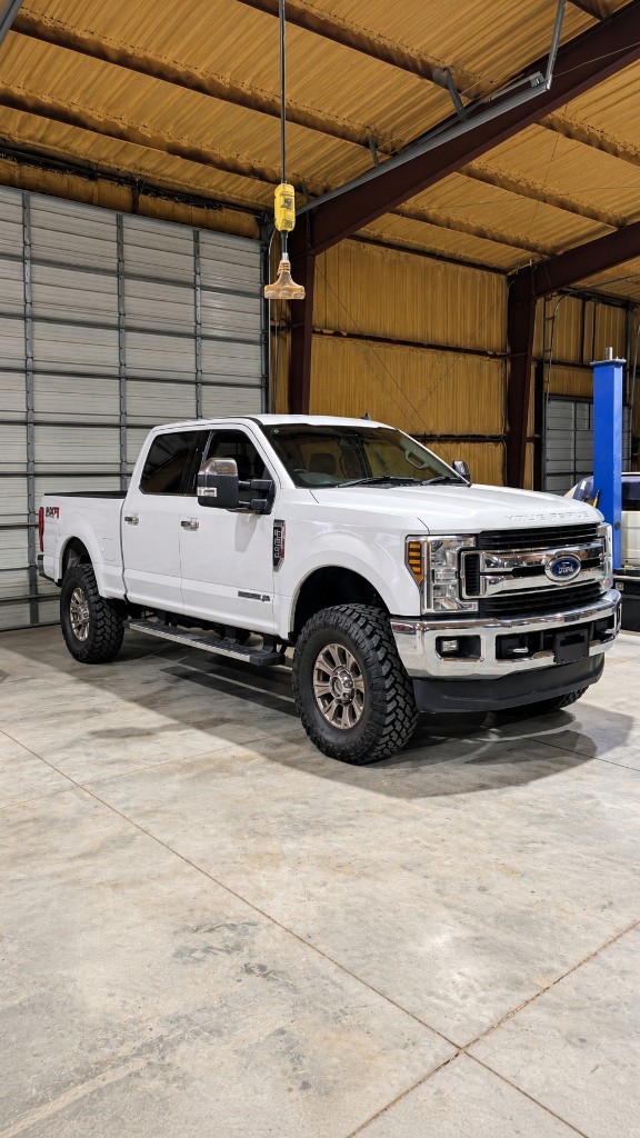 White heavy-duty crew-cab pickup inside a repair shop