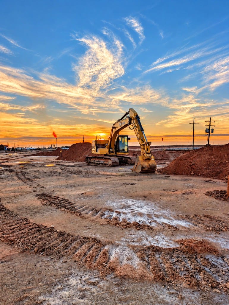 Yellow excavator on a dirt construction site at sunset
