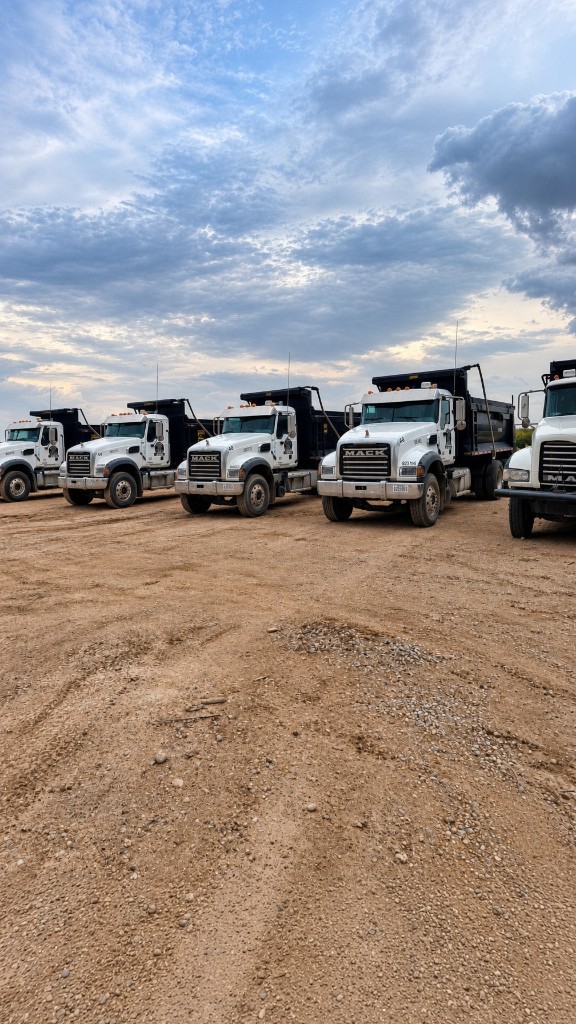 White Mack dump trucks parked in a row on a dirt yard